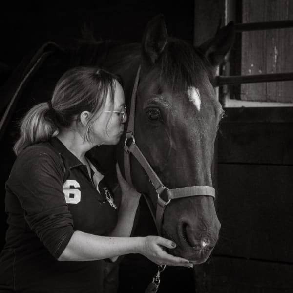 Cavalière embrassant le bout du nez de son cheval noir dans l’écurie