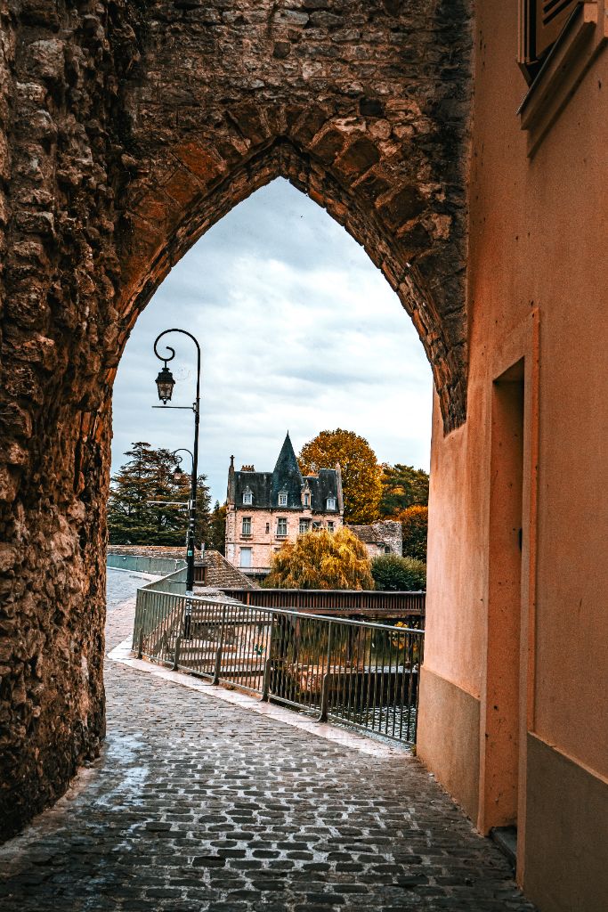 À travers l'arc brisé d'une porte de pierre, perspective vers le manoir au bord du Loing