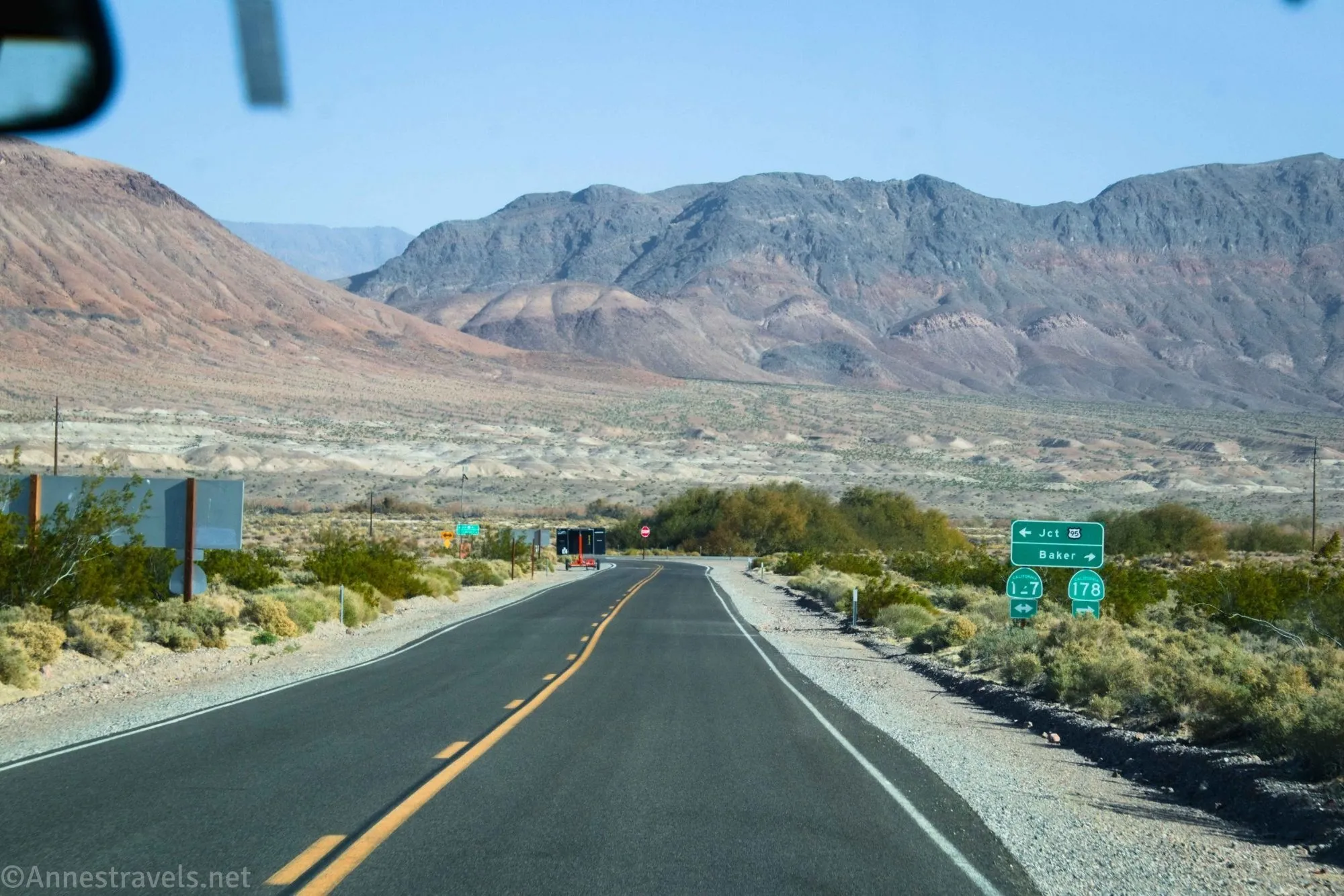 A paved road and signs below desert mountains