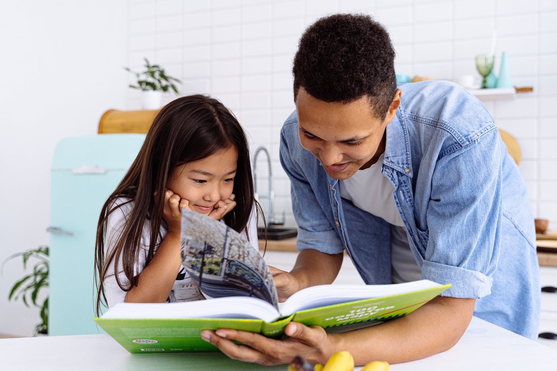 photograph of a child reading a book with her father