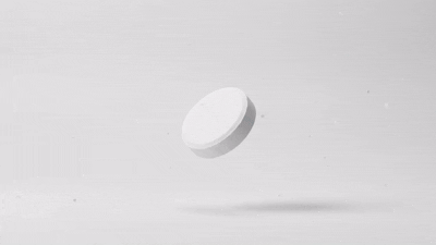 Hand dropping an effervescent tablet into a glass of water in a bright, sunlit kitchen