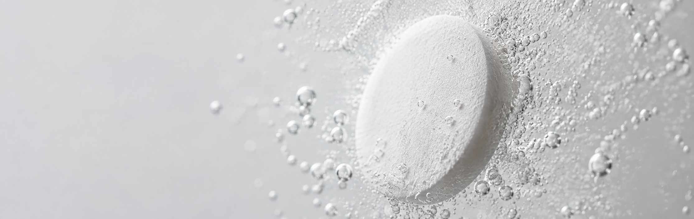 Hand dropping an effervescent tablet into a fizzing glass of water in a sunlit kitchen