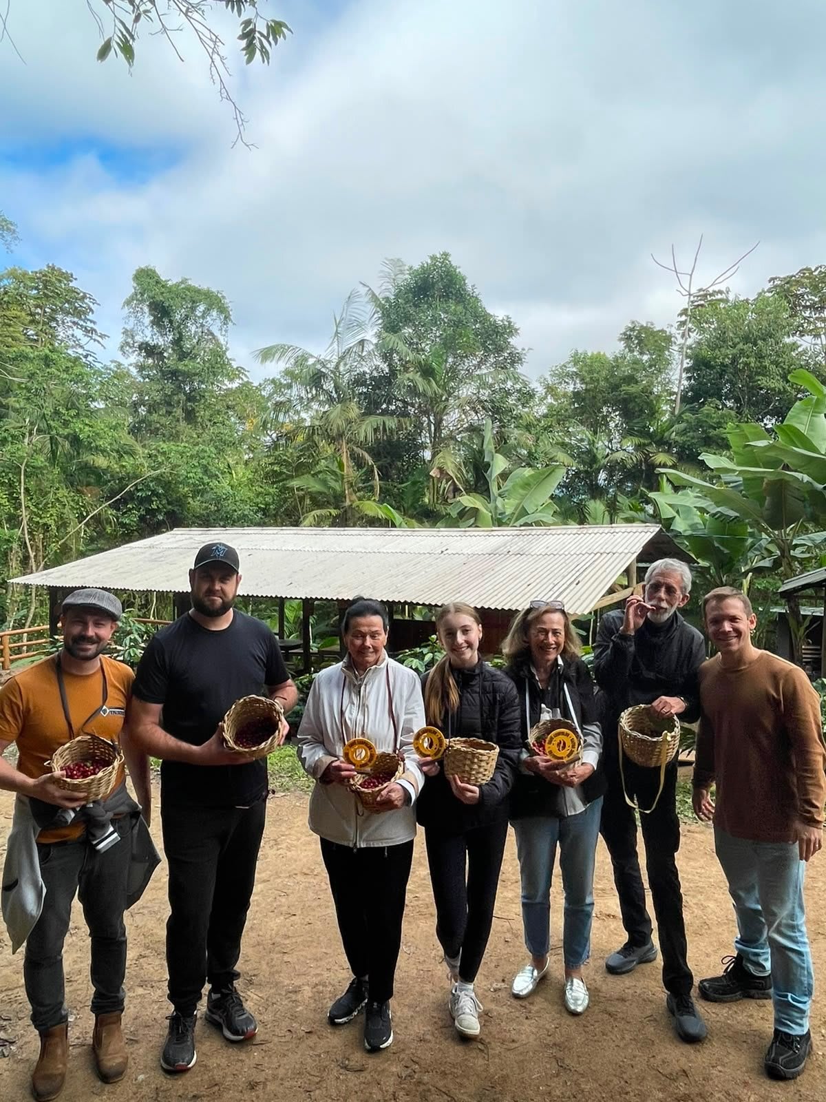 Grupo em visita a uma fazenda de café, cada pessoa segurando um cesto com cerejas colhidas