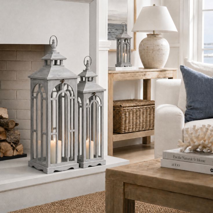 Set of three wooden lanterns with white-wash finish and aged brass clasps displayed on a floor.