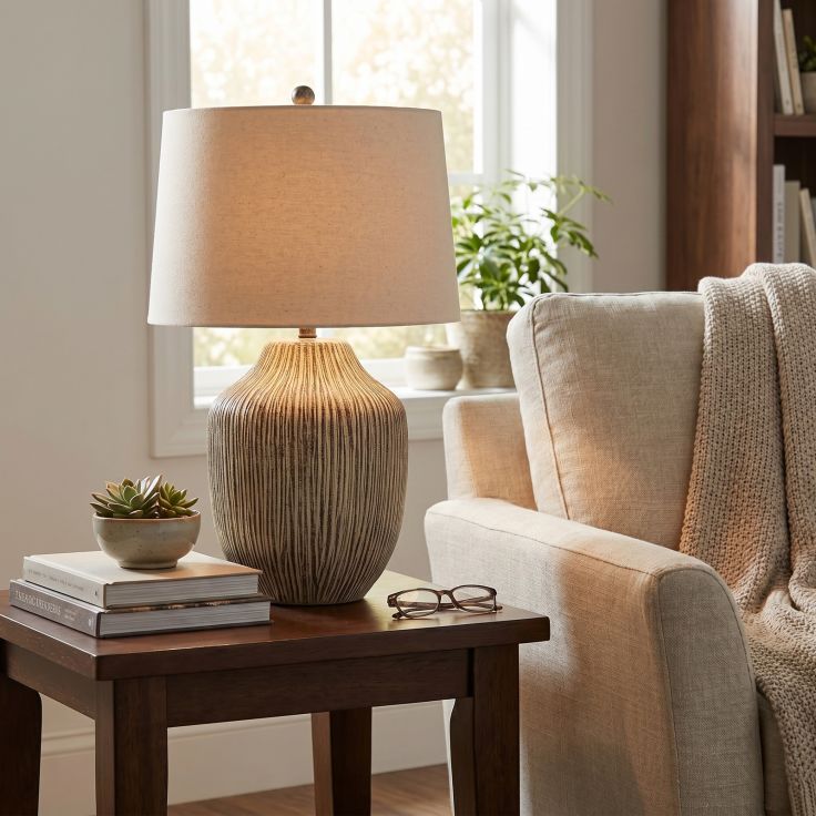 A close-up of an ochre-coloured carved textured ceramic table lamp with a cream linen shade on a side table.