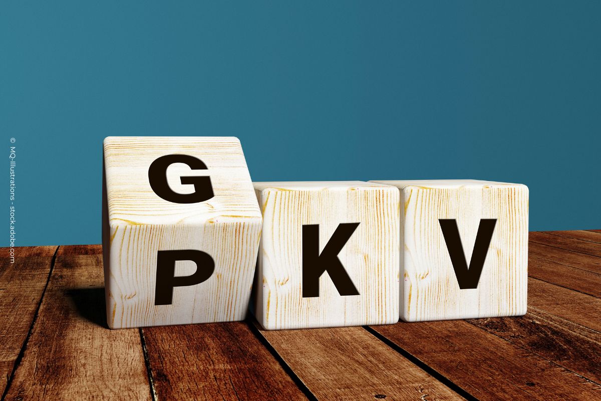 Drei Holzklötze mit den Buchstaben "G", "P", "K" und "V". Die Klötze stehen auf einer hölzernen Tischplatte vor einem blauen Hintergrund.