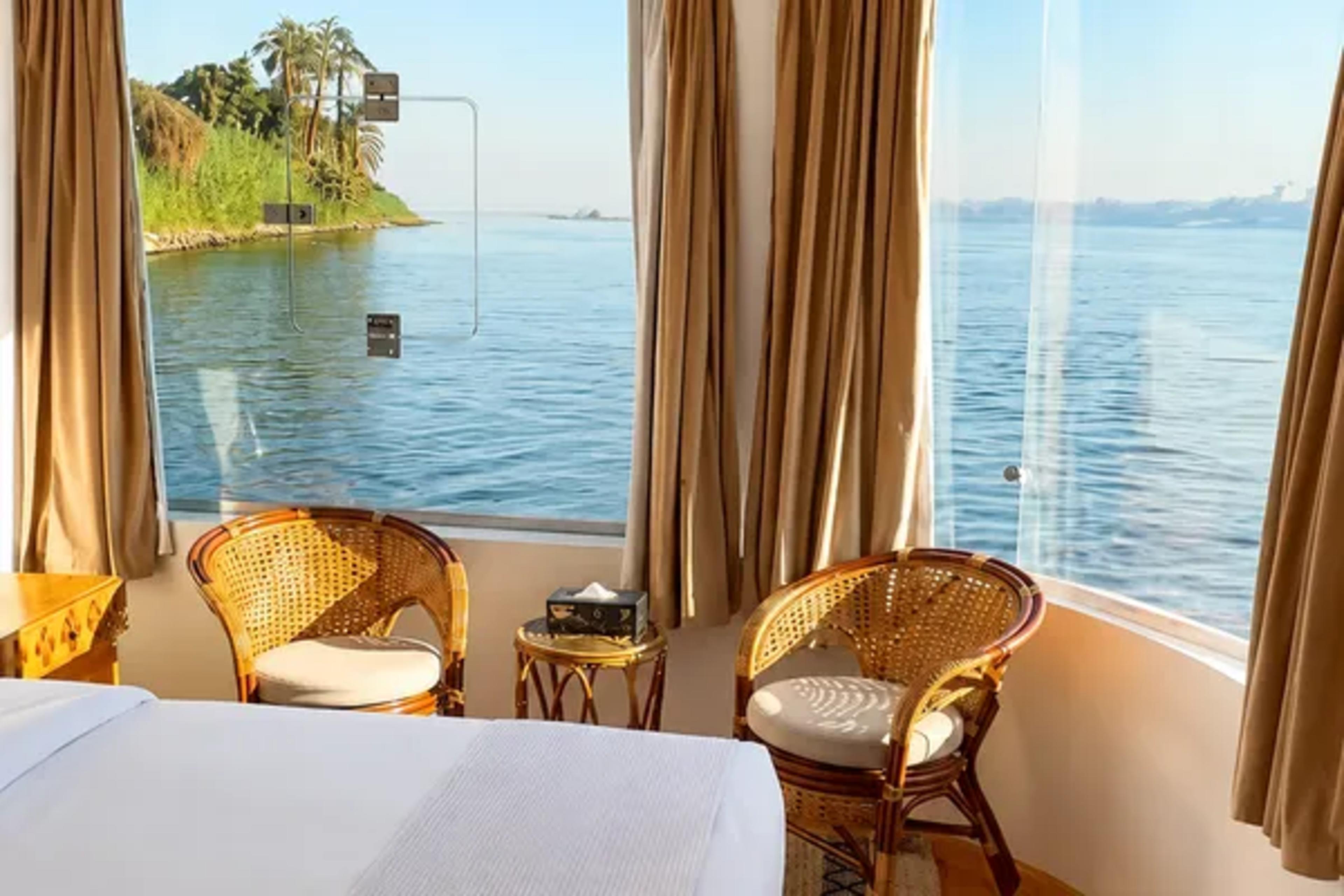 Nile-facing corner cabin on a river cruise boat, with floor-to-ceiling windows looking onto the river and a palm-fringed island