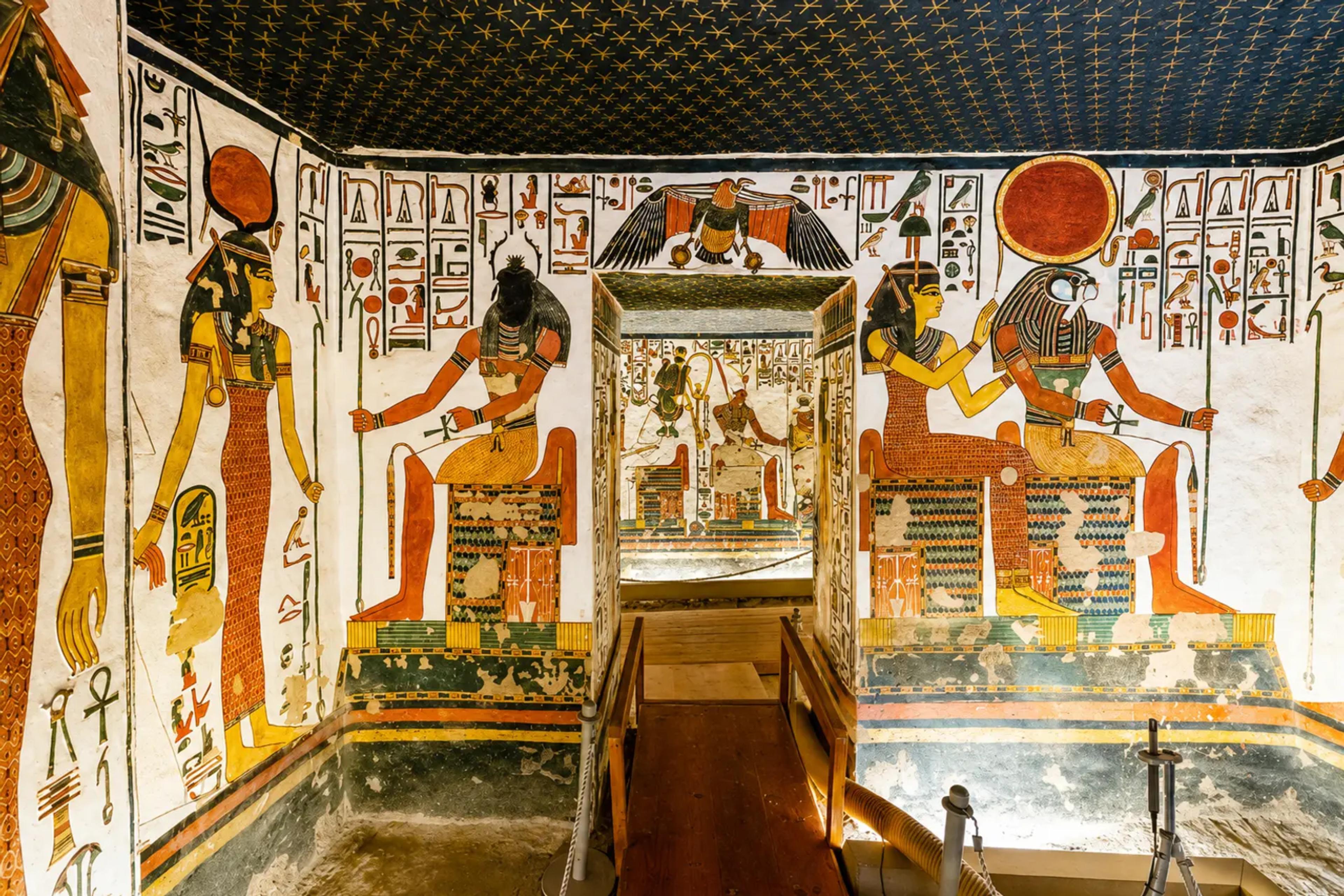 ainted burial chamber inside the tomb of Nefertari in the Valley of the Queens, with the goddess Hathor, an enthroned Osiris, the goddess Isis presenting Queen Nefertari to a falcon-headed Ra-Horakhty, hieroglyph friezes on white plaster, and a ceiling of golden stars on indigo overhead.