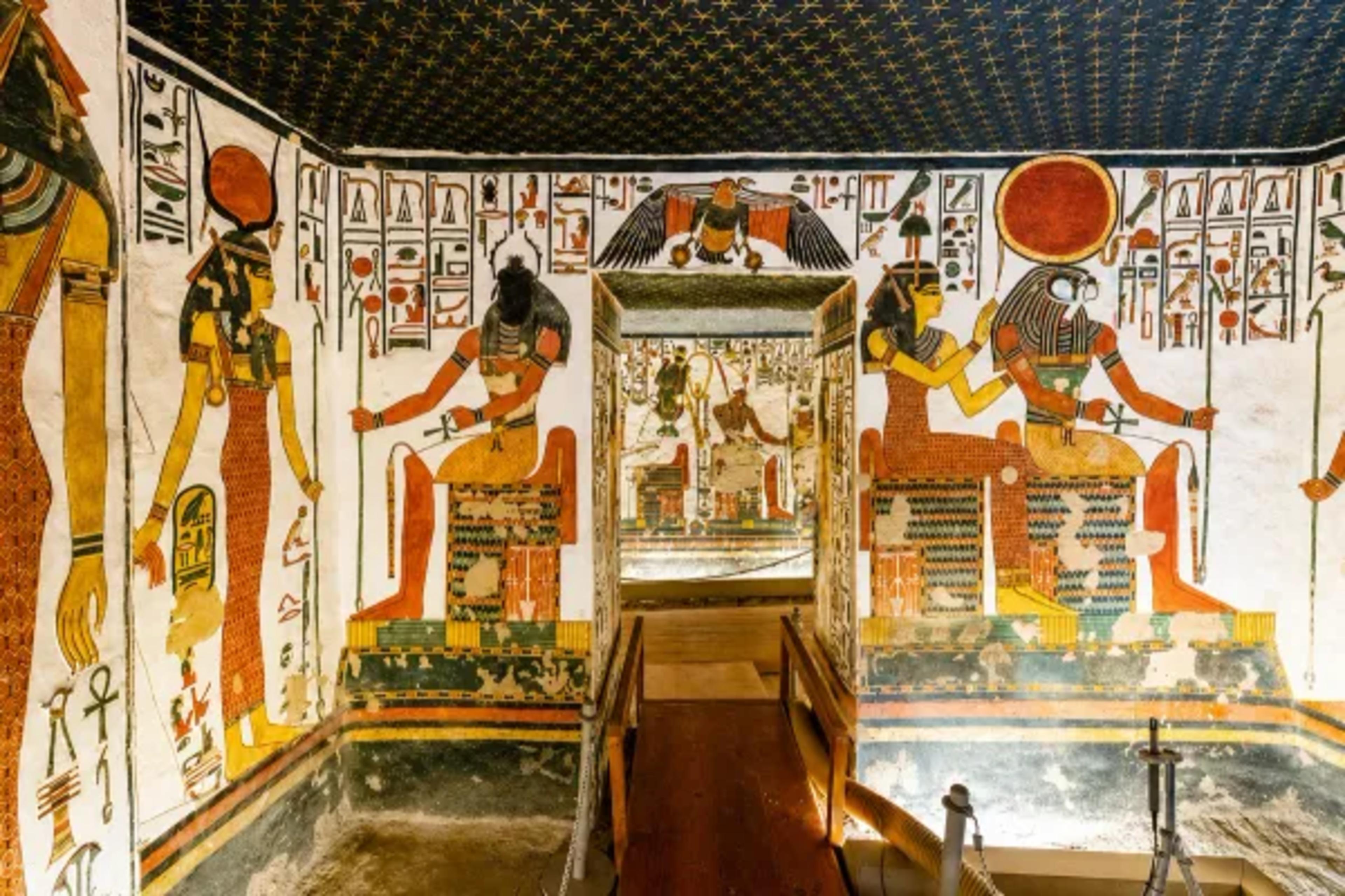ainted burial chamber inside the tomb of Nefertari in the Valley of the Queens, with the goddess Hathor, an enthroned Osiris, the goddess Isis presenting Queen Nefertari to a falcon-headed Ra-Horakhty, hieroglyph friezes on white plaster, and a ceiling of golden stars on indigo overhead.