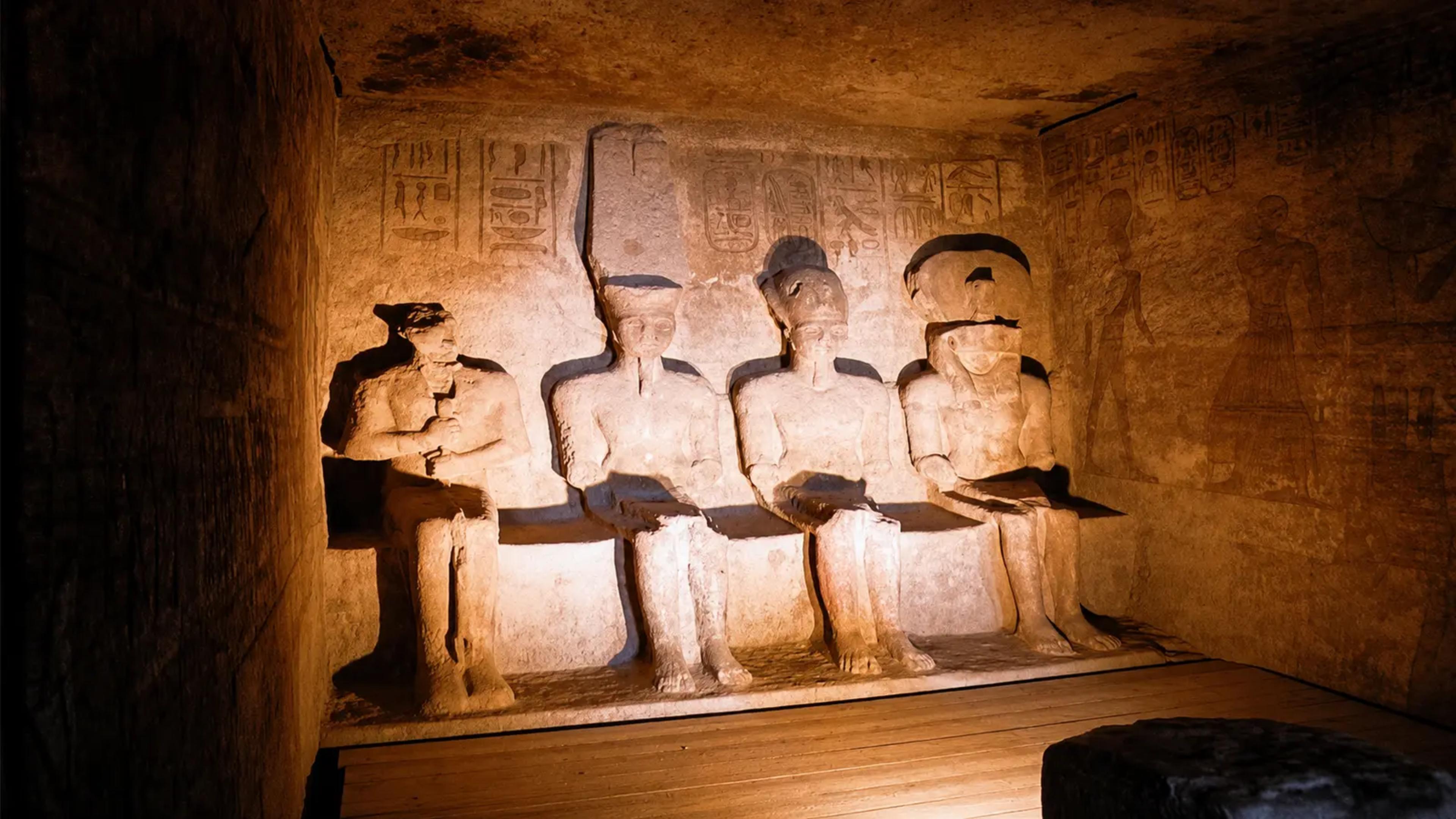 Sun-lit inner sanctuary of the Great Temple of Abu Simbel, with the four seated rock-cut statues of Ptah, Amun-Ra, the deified Ramesses II, and Ra-Horakhty against a hieroglyph-carved wall.