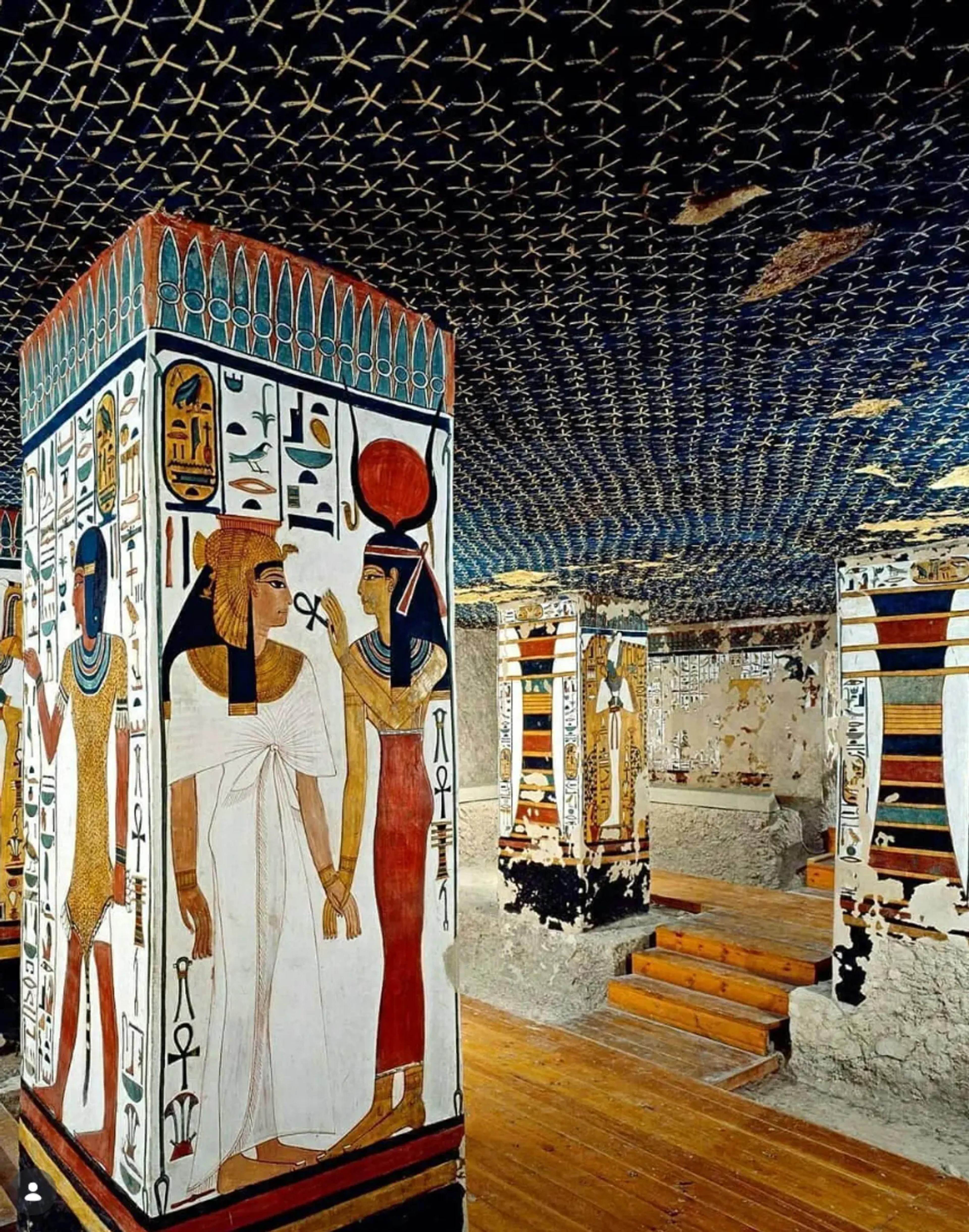 Interior of the tomb of Nefertari in the Valley of the Queens, with a painted column showing Queen Nefertari led by the goddess Isis beneath a vaulted ceiling of golden stars on indigo.