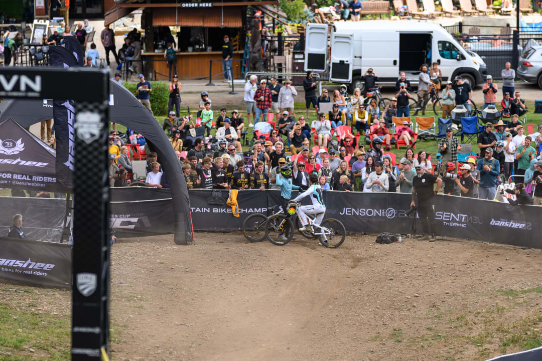 Two riders roll through the finish corral at Purgatory with the crowd packed along the fence