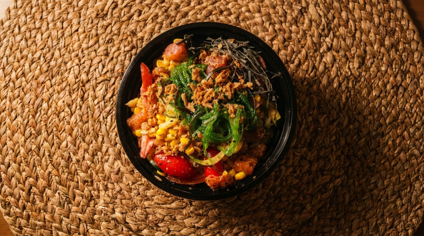 Overhead view of a colorful poke bowl with tuna, corn, seaweed, and crispy onions on a woven mat.