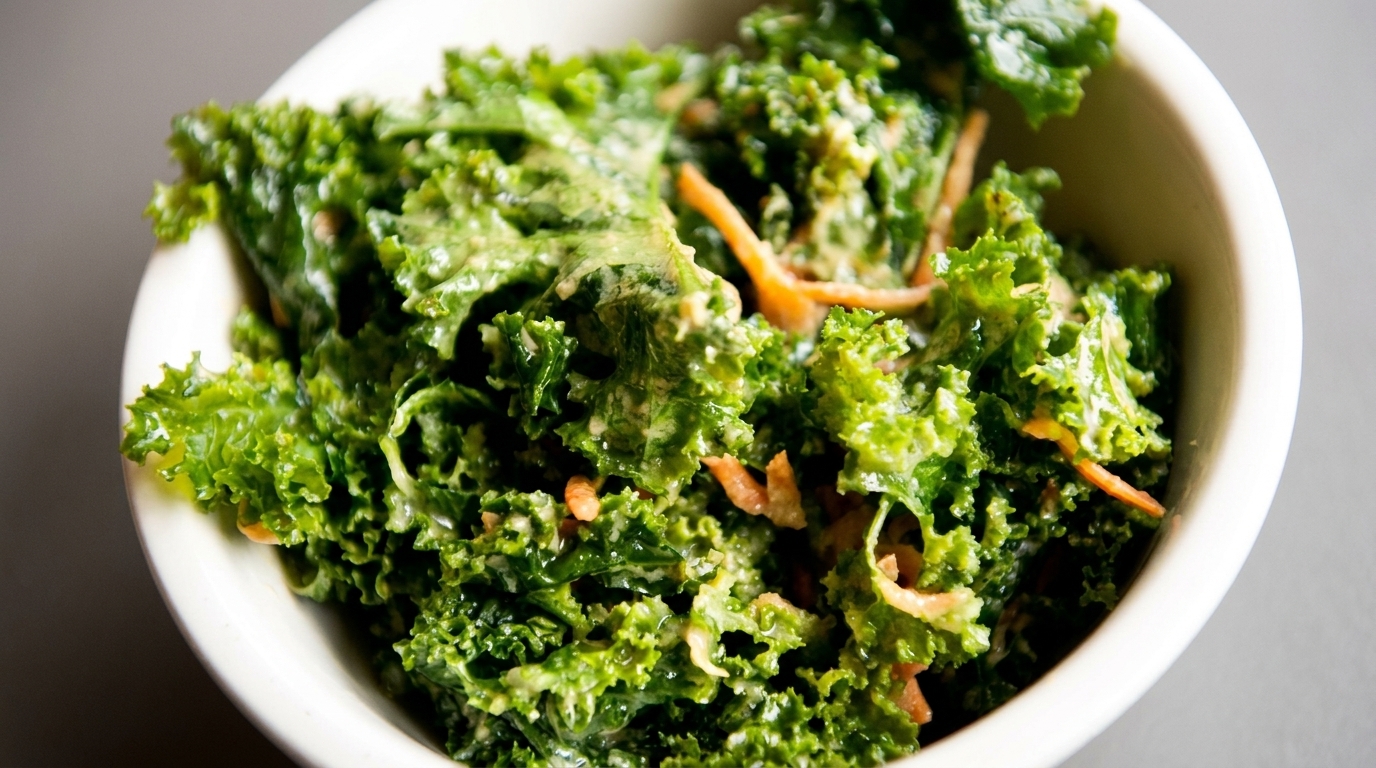Close-up of a vibrant green kale salad with shredded carrots and creamy dressing in a white bowl.