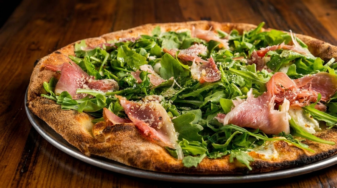 A whole pizza topped with fresh arugula, prosciutto, and grated cheese on a metal pan.
