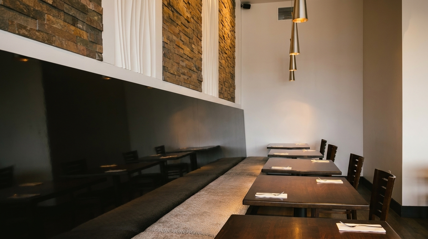 Modern restaurant interior with dark wooden tables, a long banquette, and stone accent walls.