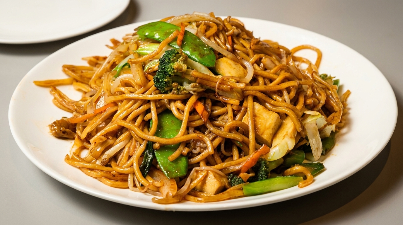 A white plate filled with vegetable lo mein noodles, including broccoli, snap peas, and carrots.