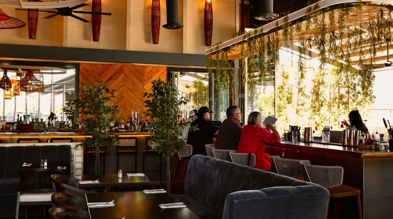 Restaurant interior with patrons at a bar, lush greenery, and modern decor with wooden accents.