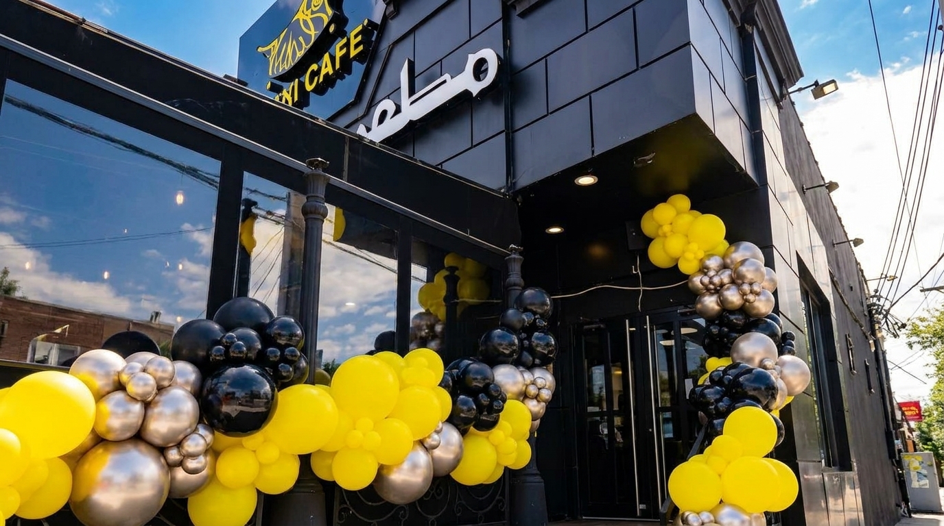 Exterior of a modern black building with large windows, decorated with yellow, silver, and black balloons.