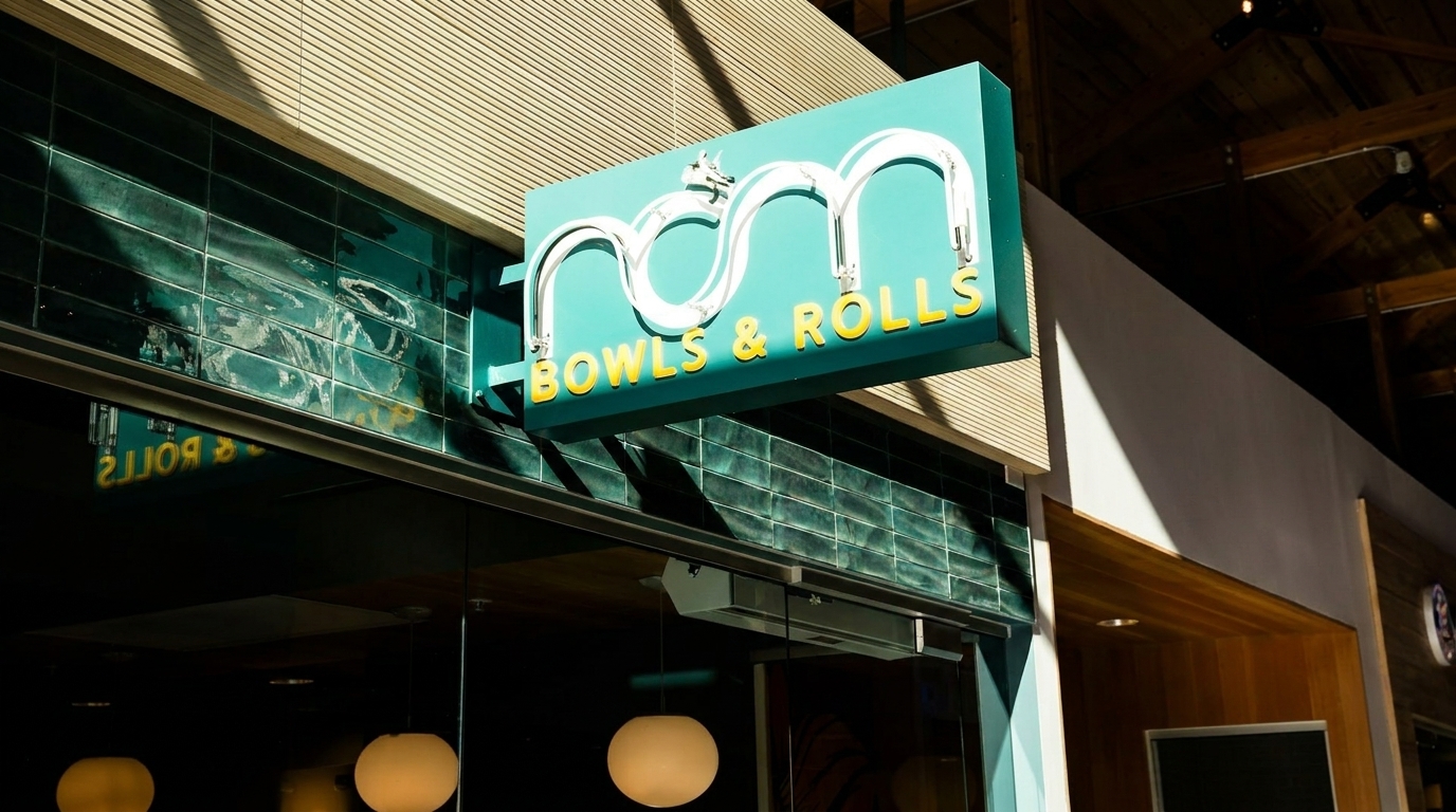A teal "Bowls & Rolls" sign with white neon letters hangs above a restaurant entrance.