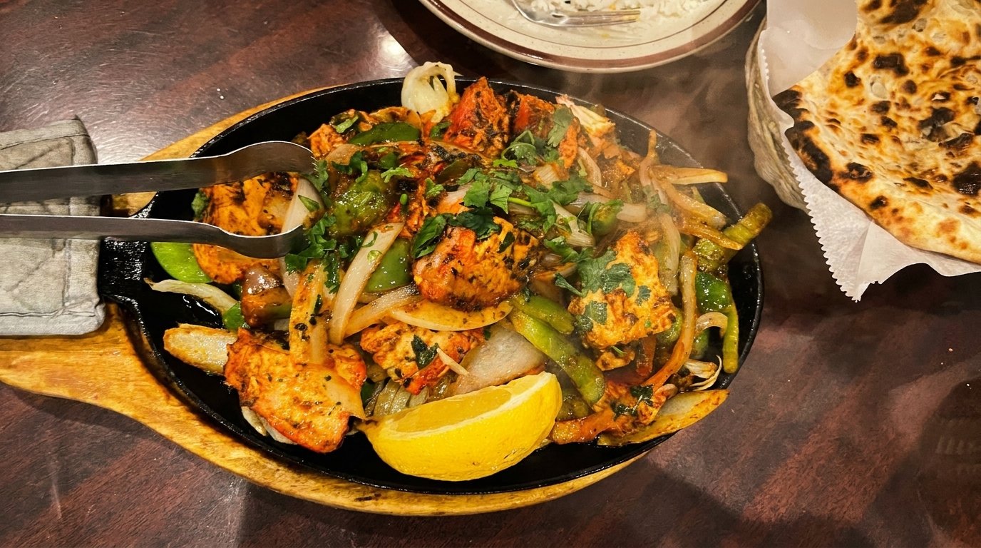 Sizzling chicken tikka with onions, peppers, cilantro, and a lemon wedge, served with naan.