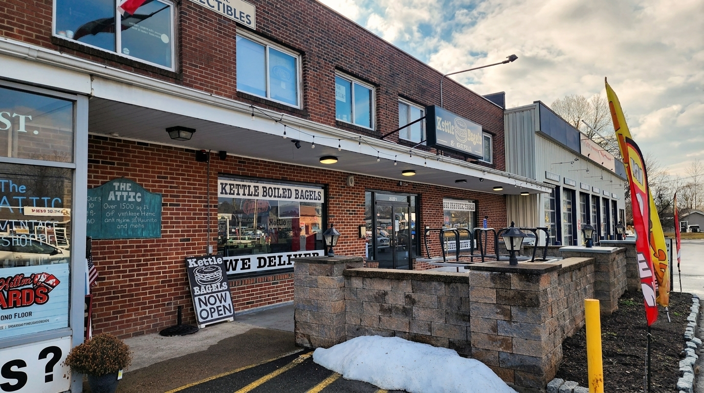 Exterior of Kettle Boiled Bagels, a brick building with a "Now Open" sign and snow on the ground.