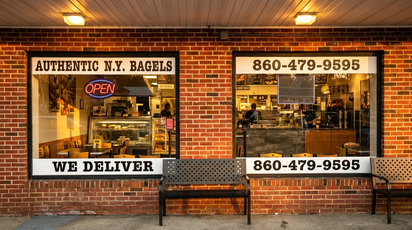 Exterior of a brick bagel shop with large windows, an "OPEN" sign, and a delivery number.