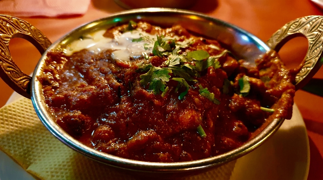 Rich red curry with cream and fresh cilantro in a decorative metal bowl.