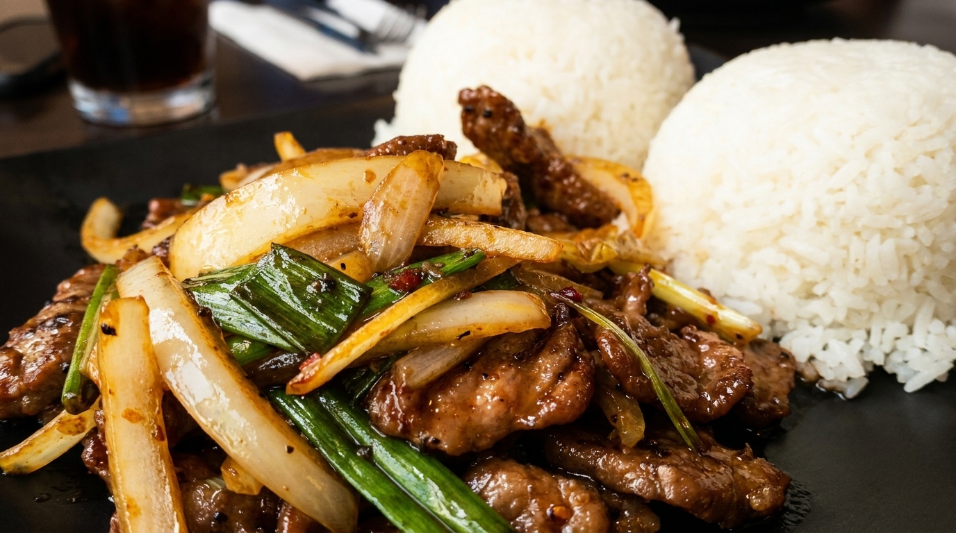 Stir-fried beef with onions and green scallions, served with two mounds of white rice.