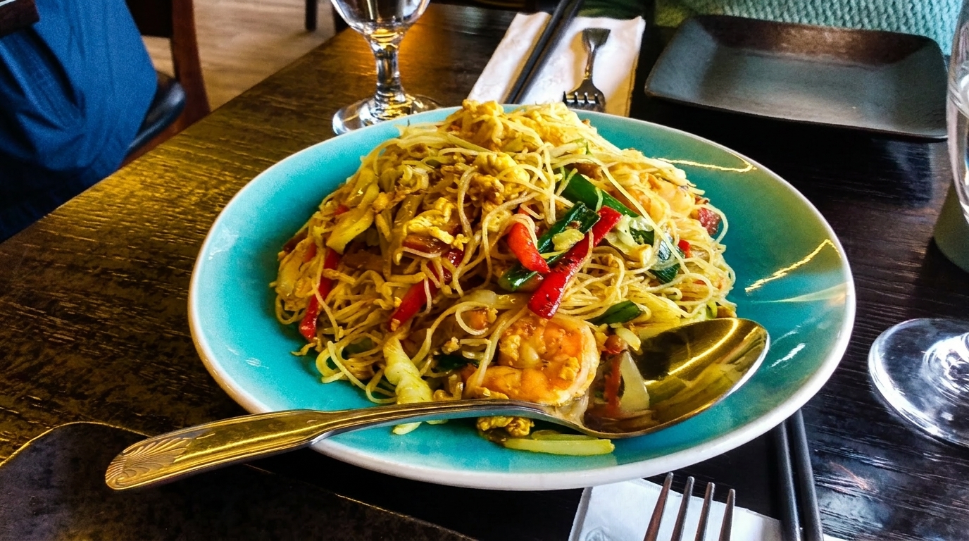 A vibrant plate of shrimp pad thai with noodles, vegetables, and egg on a dark wooden table.