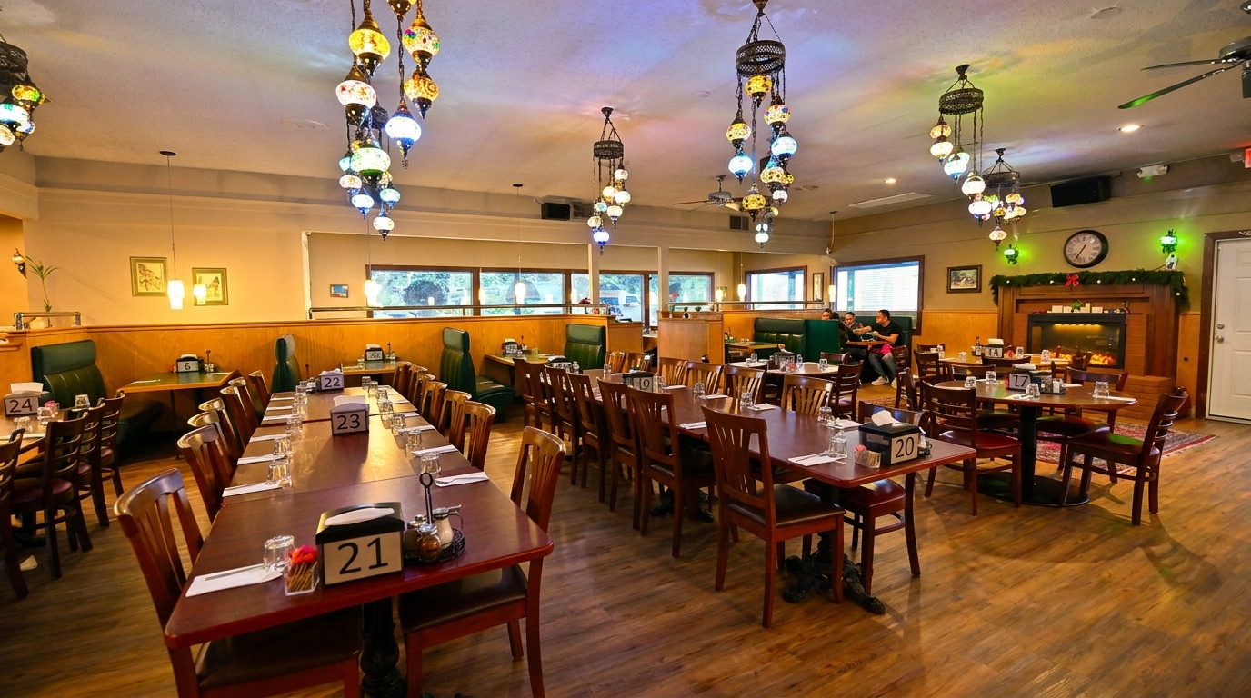 A restaurant dining room with long tables, booths, and colorful hanging lamps, with a fireplace at the back.