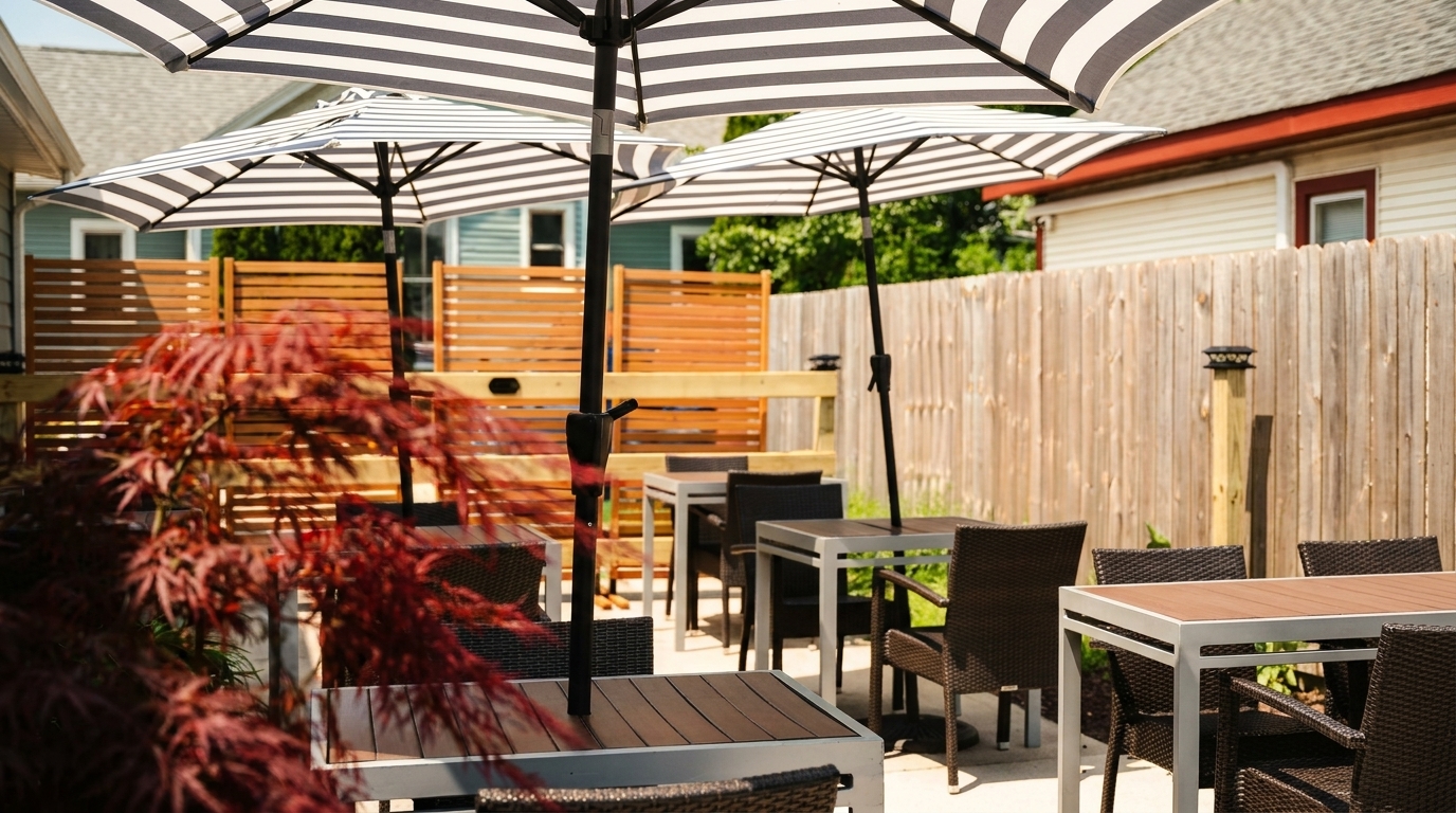 Outdoor patio dining area with striped umbrellas, modern tables, wicker chairs, and a wooden fence.