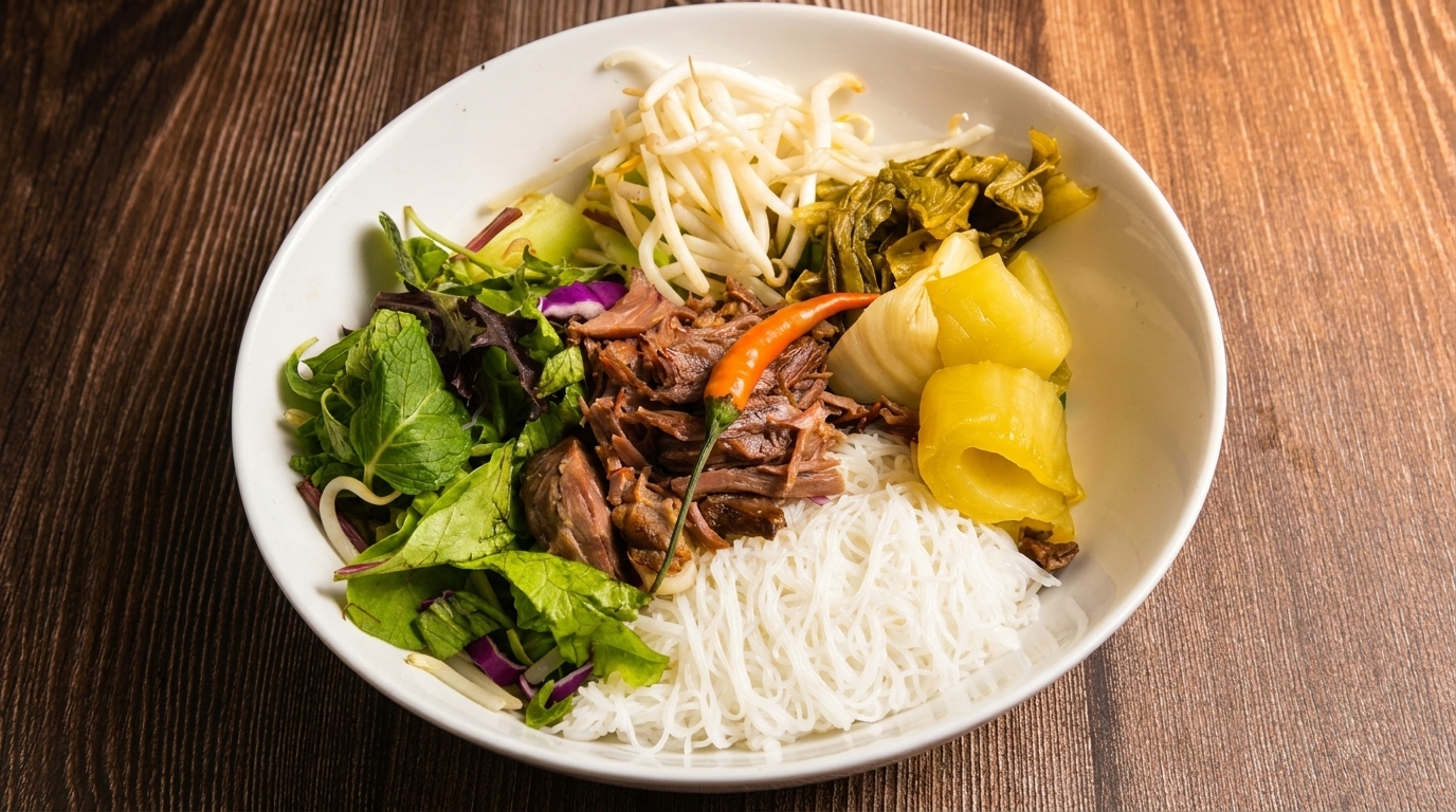 A white bowl filled with vermicelli noodles, shredded meat, bean sprouts, and greens on a wooden table.