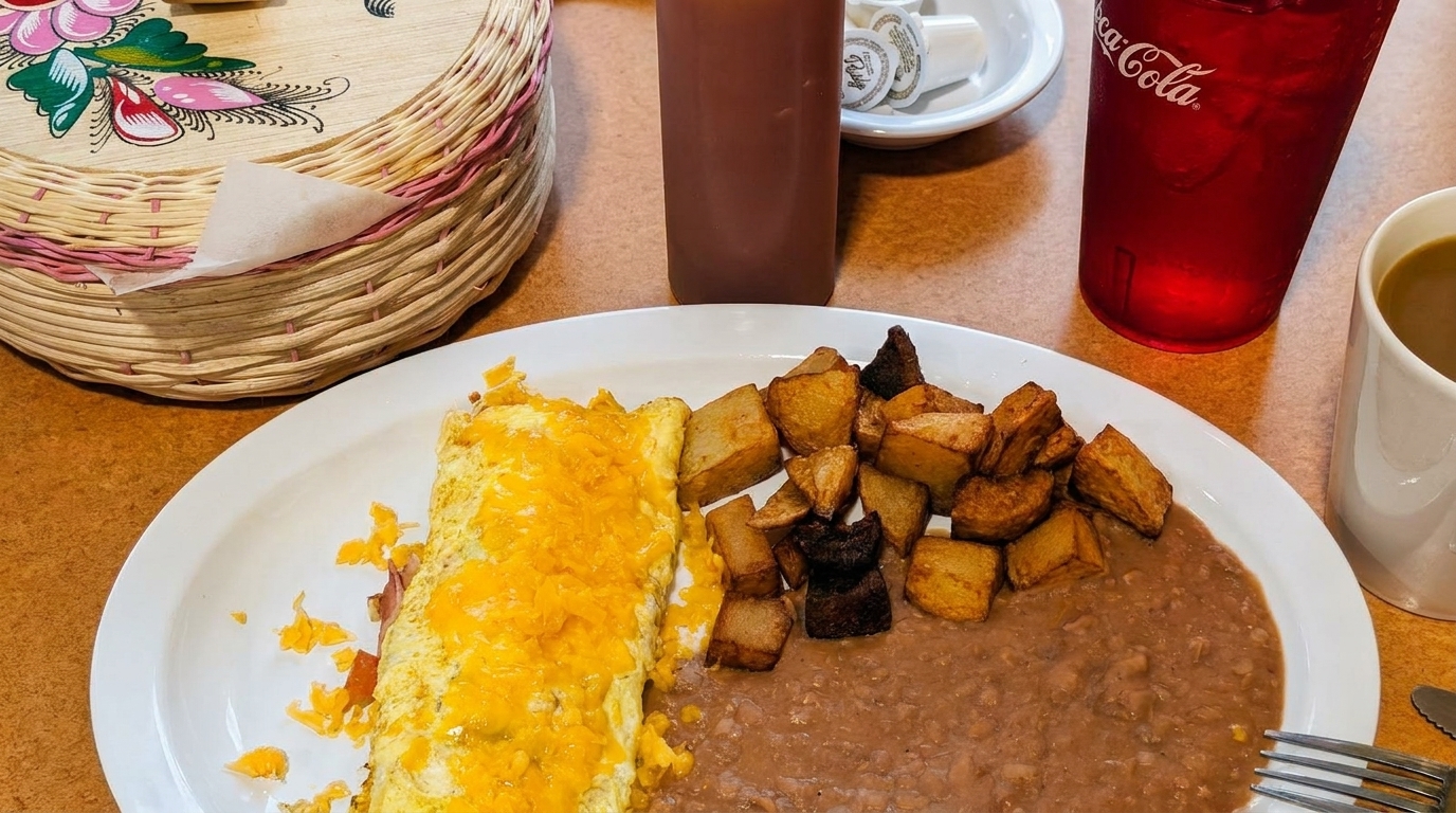A breakfast plate with a cheese omelet, home fries, refried beans, and drinks on a table.