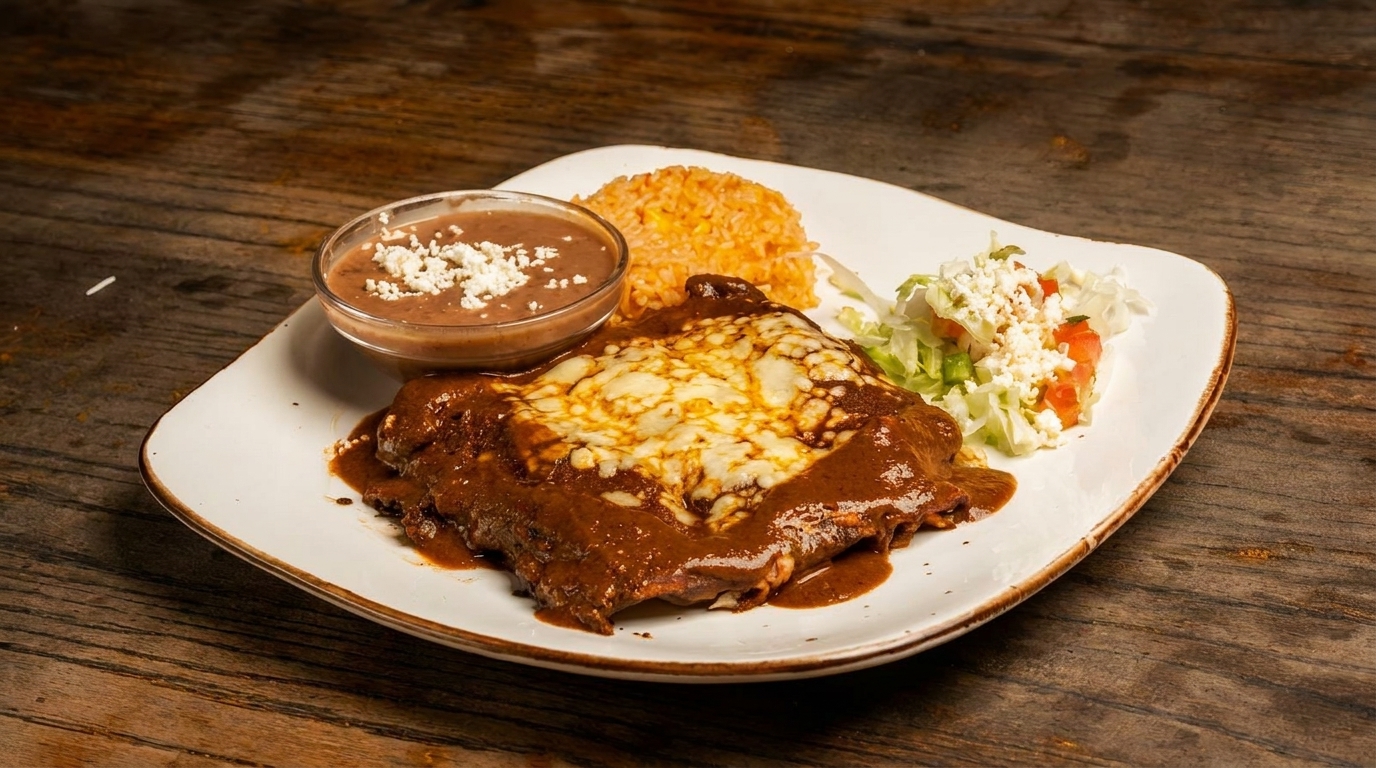 A plate of enchiladas covered in mole sauce and melted cheese, with rice, refried beans, and salad.