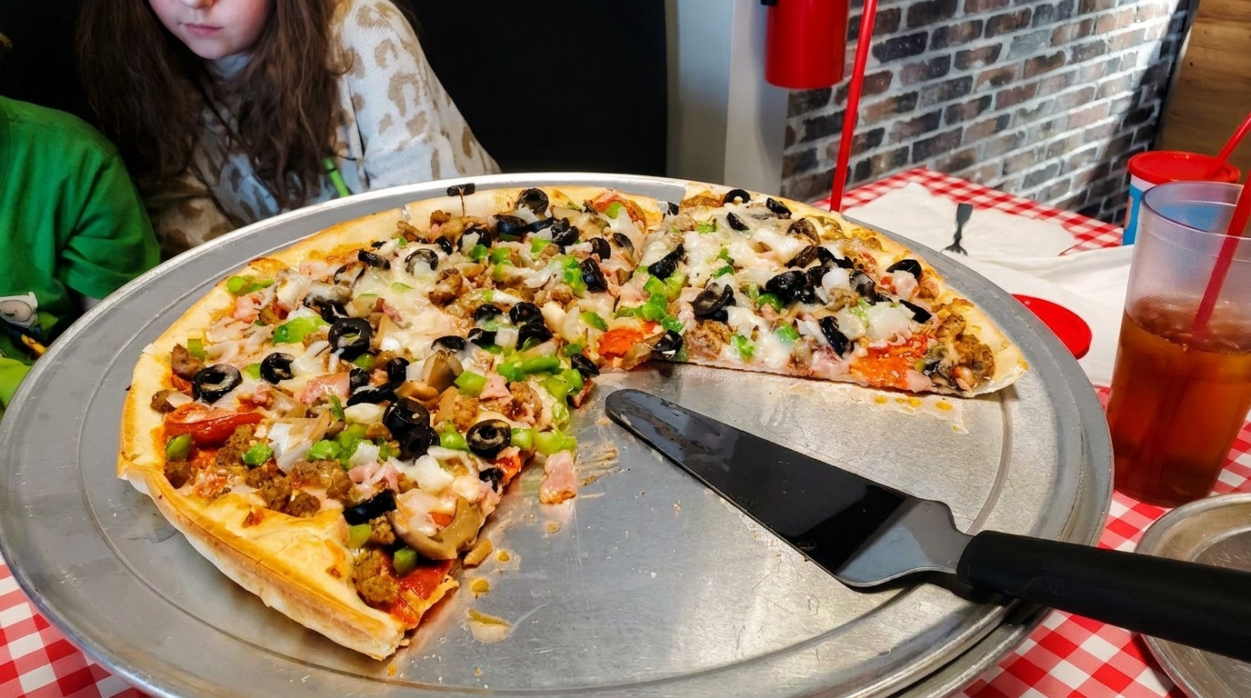 A large pizza with multiple toppings, including olives, peppers, and sausage, on a metal tray.