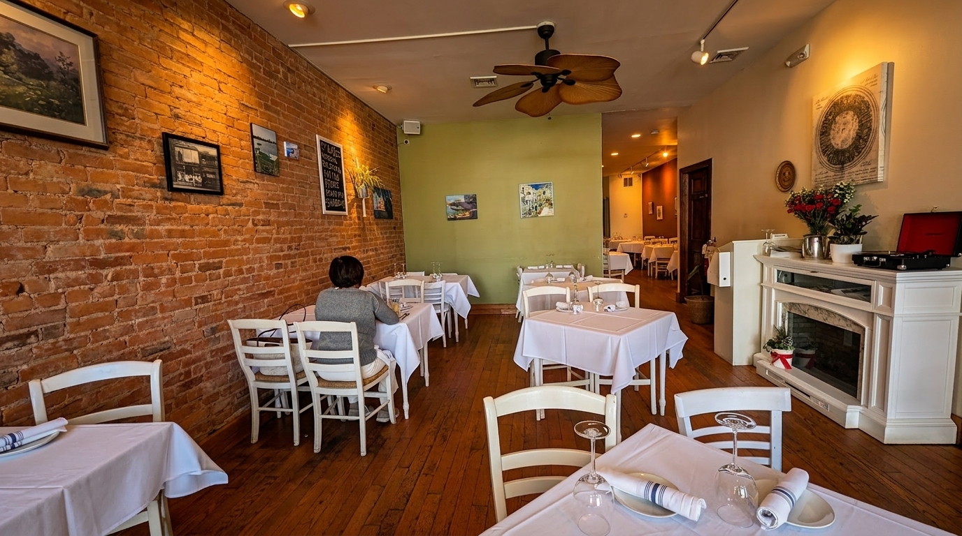 A restaurant dining room with brick walls, white-clothed tables, and a person seated at a table.