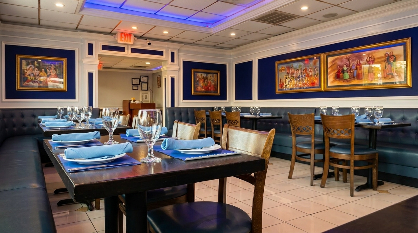 Restaurant interior with blue booths, wooden chairs, set tables, and framed artwork on blue walls.