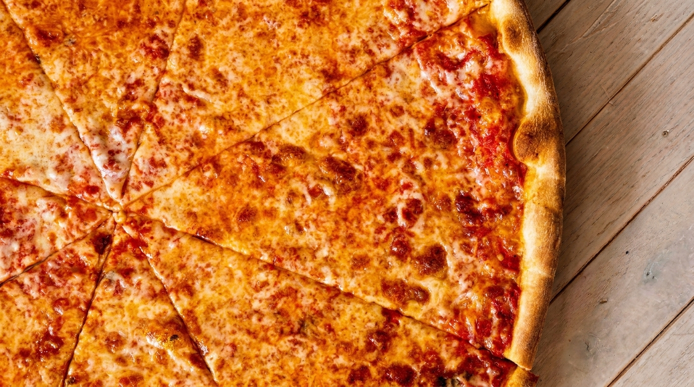 Close-up of a freshly baked cheese pizza, sliced into wedges, on a light wooden table.