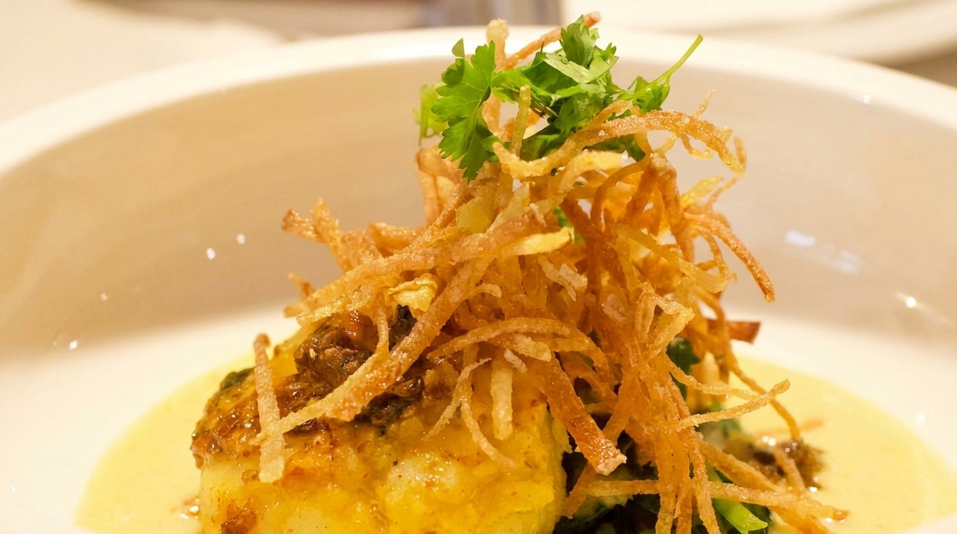 Close-up of a gourmet dish with crispy fried potato strings, cilantro, and a creamy sauce.