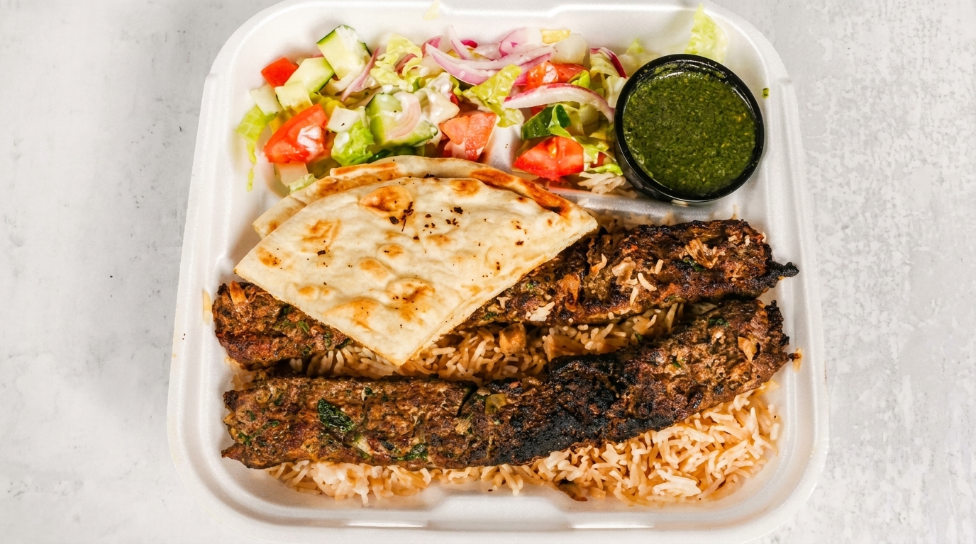 Two grilled kebabs on rice with naan bread, a side salad, and green sauce in a takeout container.