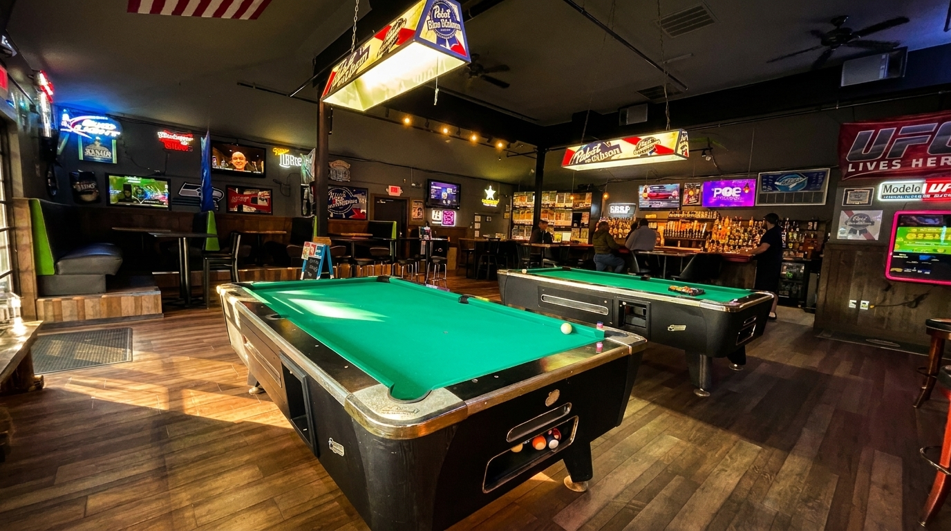 A lively bar interior with two pool tables, a long bar, and multiple TVs showing sports.