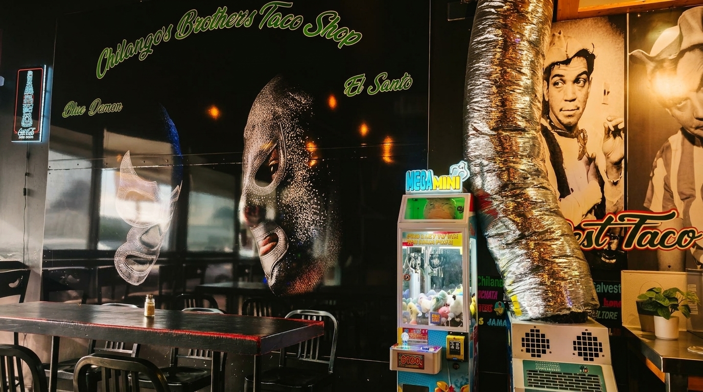 Interior of Chilangos Brothers Taco Shop with wrestling mask murals, a claw machine, and black tables.