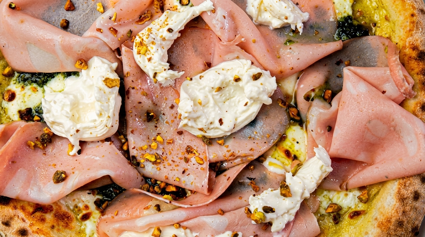 Close-up of a pizza topped with mortadella, burrata cheese, pesto, and crushed pistachios.