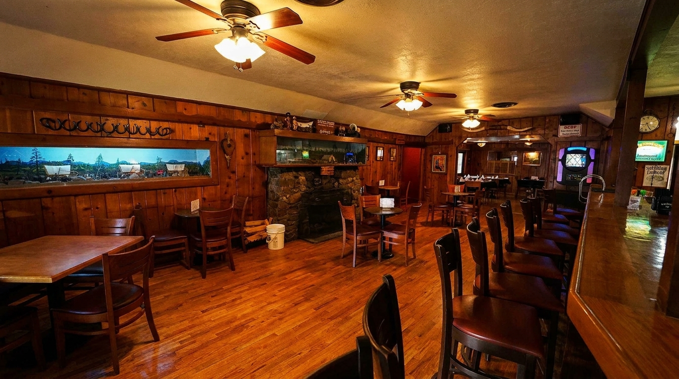 Rustic restaurant interior with wood-paneled walls, a stone fireplace, tables, chairs, and a bar.