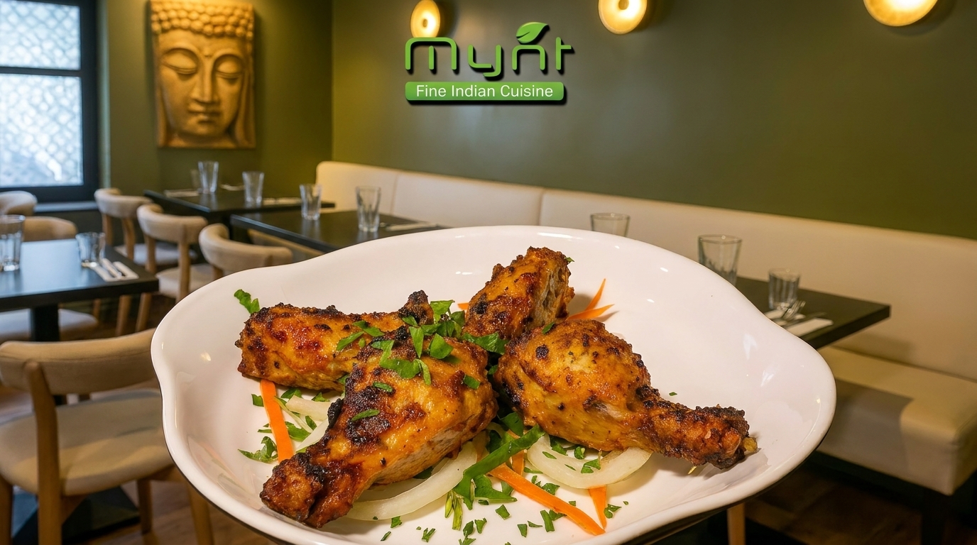 Four chicken drumsticks on a white plate with onions and herbs, in a restaurant setting.