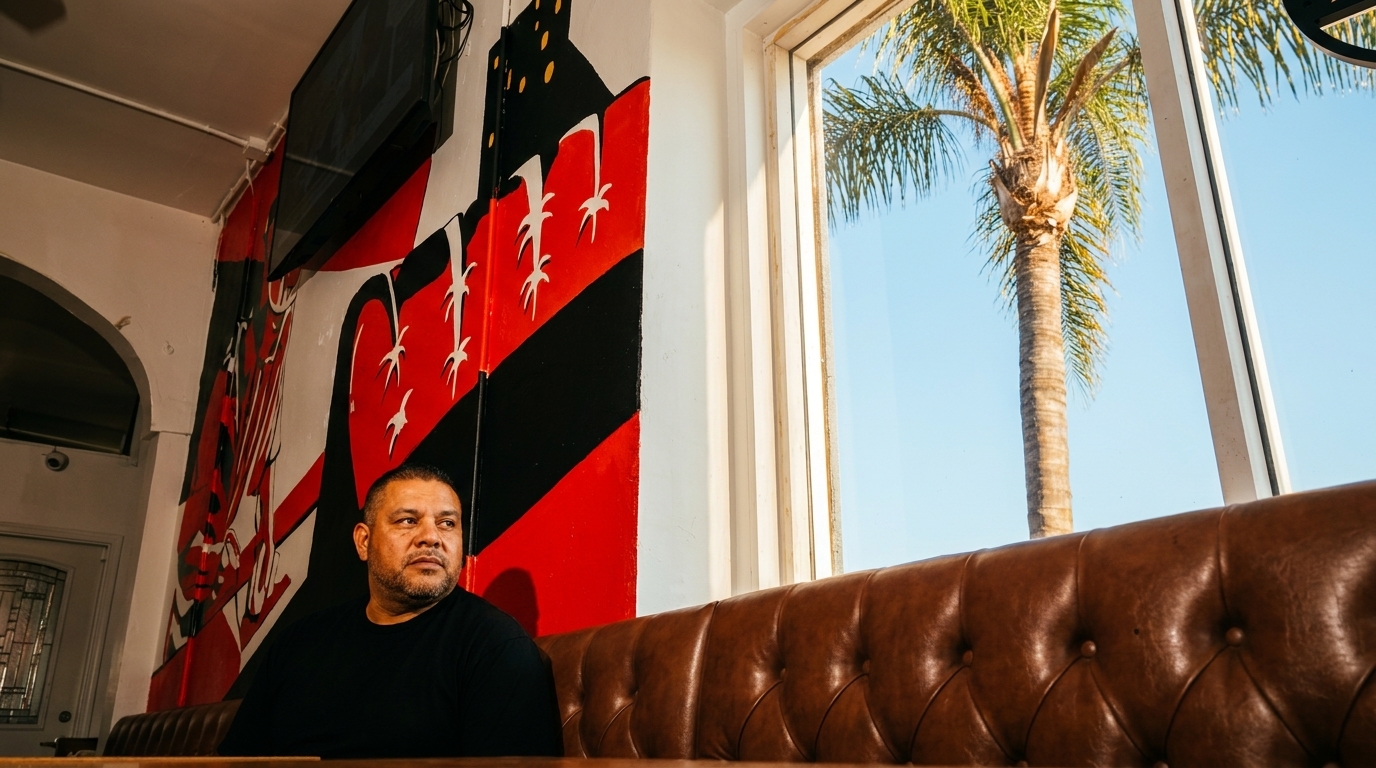 Man sitting on a brown leather booth next to a window with a palm tree outside.