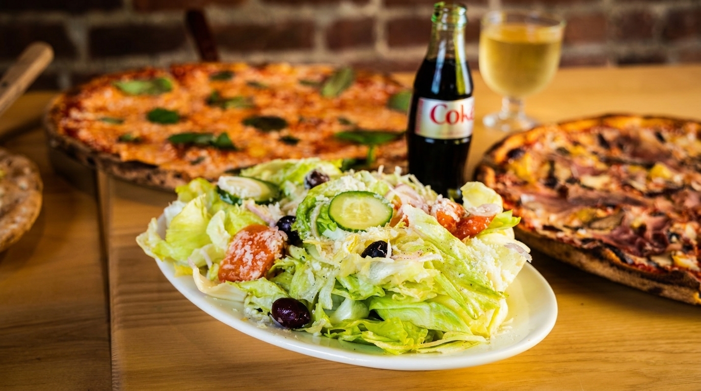 Fresh salad with two pizzas, a Coke bottle, and white wine on a wooden table.