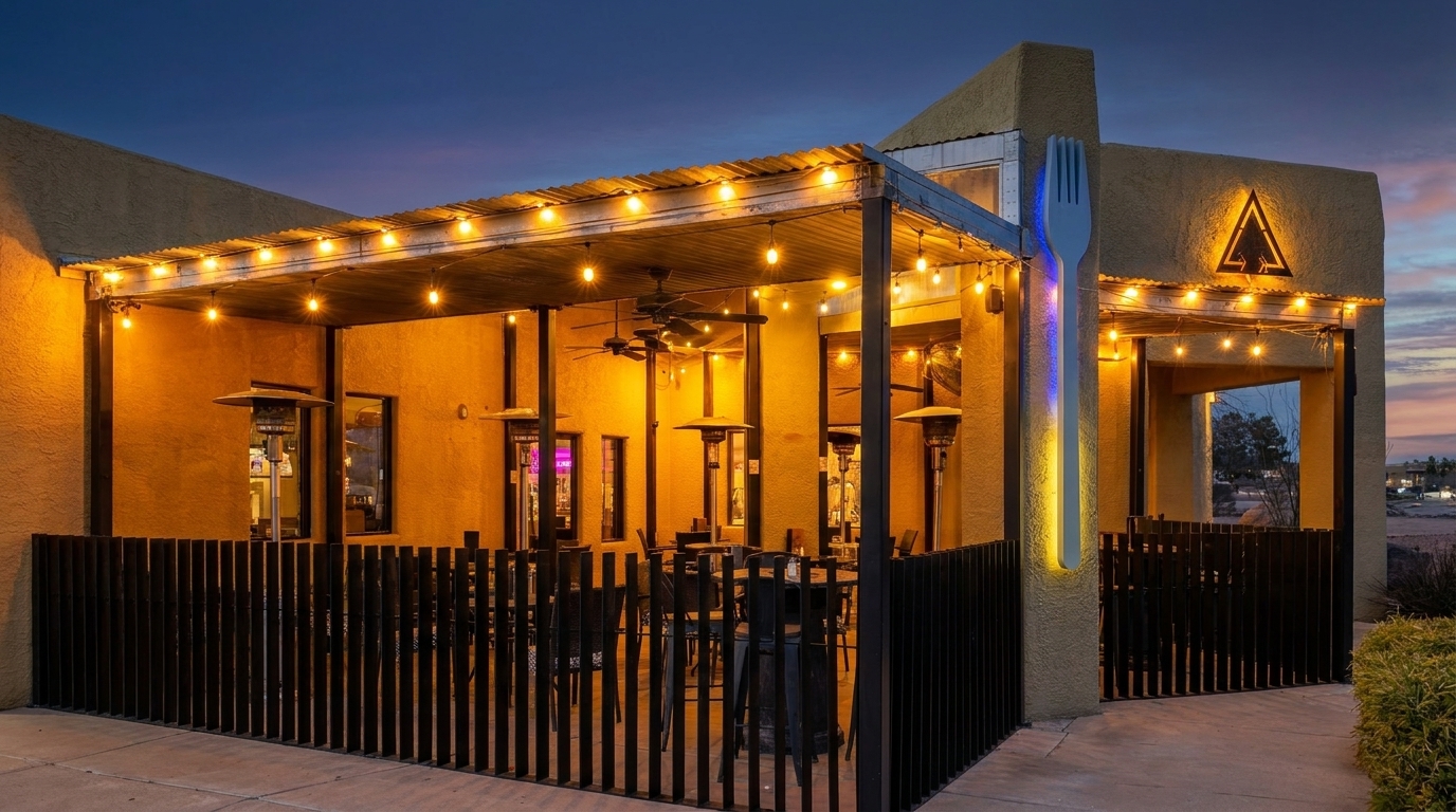 Restaurant patio at dusk with string lights, outdoor heaters, and a large fork sculpture.