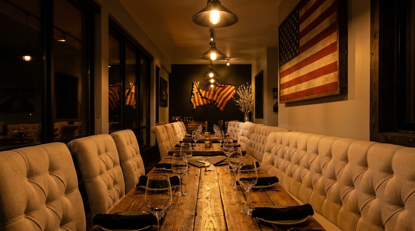 Long dining table with tufted benches, set with glasses and plates, under pendant lights and American flags.